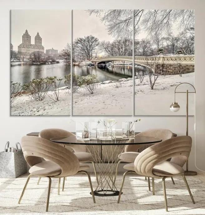 The Bow Bridge in Central Park Canvas Print features a snowy scene with a bridge and city buildings in the background. This museum-quality canvas comes with a UV-protective coating and is ready to hang.