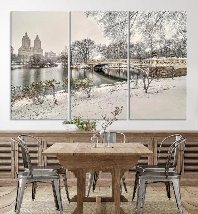 The Bow Bridge in Central Park Canvas Print features a snowy scene with a bridge and city buildings in the background. This museum-quality canvas comes with a UV-protective coating and is ready to hang.