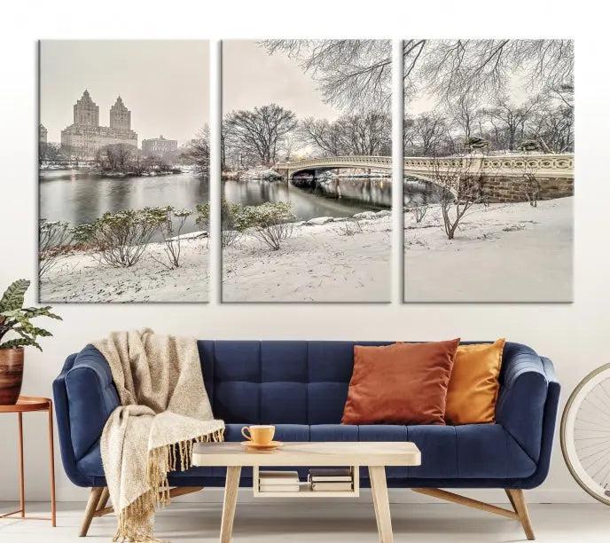 The Bow Bridge in Central Park Canvas Print features a snowy scene with a bridge and city buildings in the background. This museum-quality canvas comes with a UV-protective coating and is ready to hang.