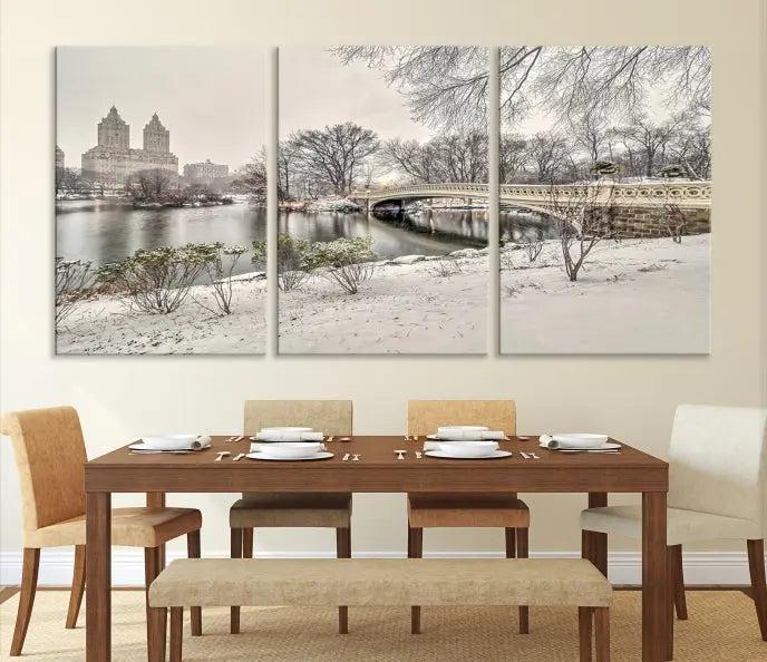 The Bow Bridge in Central Park Canvas Print features a snowy scene with a bridge and city buildings in the background. This museum-quality canvas comes with a UV-protective coating and is ready to hang.