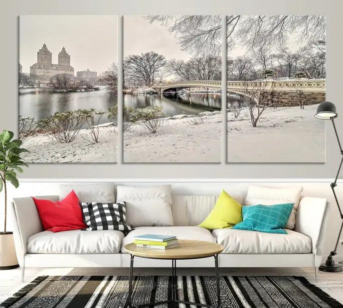 The Bow Bridge in Central Park Canvas Print features a snowy scene with a bridge and city buildings in the background. This museum-quality canvas comes with a UV-protective coating and is ready to hang.