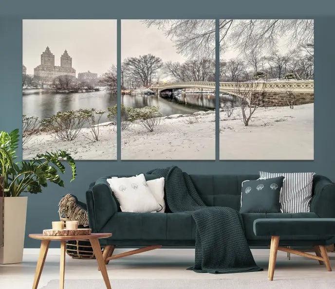 The Bow Bridge in Central Park Canvas Print features a snowy scene with a bridge and city buildings in the background. This museum-quality canvas comes with a UV-protective coating and is ready to hang.