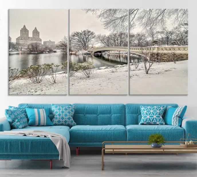 The Bow Bridge in Central Park Canvas Print features a snowy scene with a bridge and city buildings in the background. This museum-quality canvas comes with a UV-protective coating and is ready to hang.