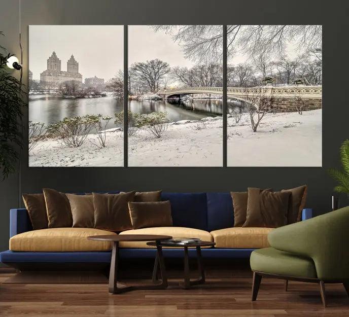 The Bow Bridge in Central Park Canvas Print features a snowy scene with a bridge and city buildings in the background. This museum-quality canvas comes with a UV-protective coating and is ready to hang.