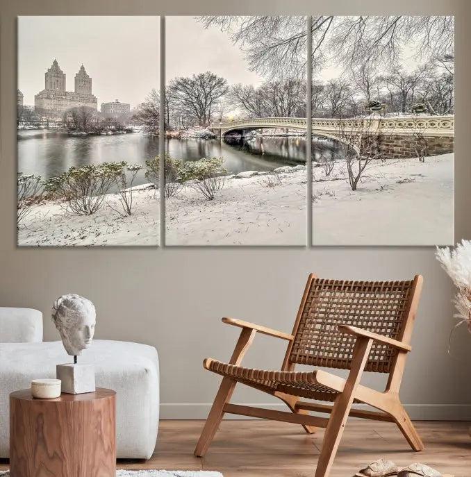 The Bow Bridge in Central Park Canvas Print features a snowy scene with a bridge and city buildings in the background. This museum-quality canvas comes with a UV-protective coating and is ready to hang.