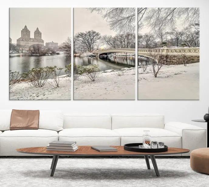 The Bow Bridge in Central Park Canvas Print features a snowy scene with a bridge and city buildings in the background. This museum-quality canvas comes with a UV-protective coating and is ready to hang.