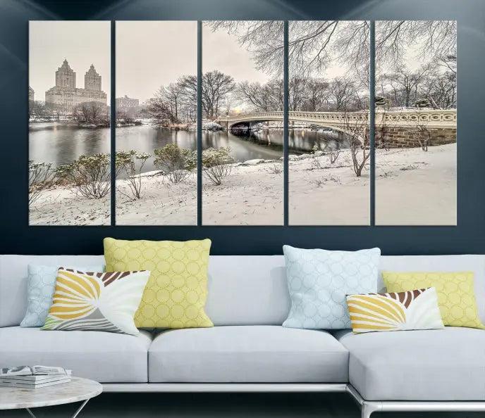 The Bow Bridge in Central Park Canvas Print features a snowy scene with a bridge and city buildings in the background. This museum-quality canvas comes with a UV-protective coating and is ready to hang.