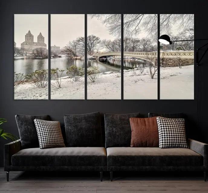 The Bow Bridge in Central Park Canvas Print features a snowy scene with a bridge and city buildings in the background. This museum-quality canvas comes with a UV-protective coating and is ready to hang.