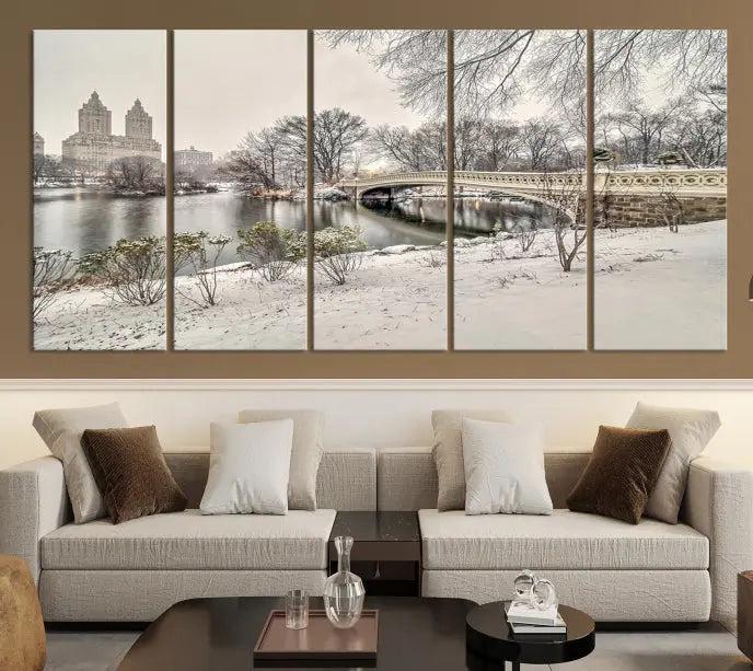 The Bow Bridge in Central Park Canvas Print features a snowy scene with a bridge and city buildings in the background. This museum-quality canvas comes with a UV-protective coating and is ready to hang.