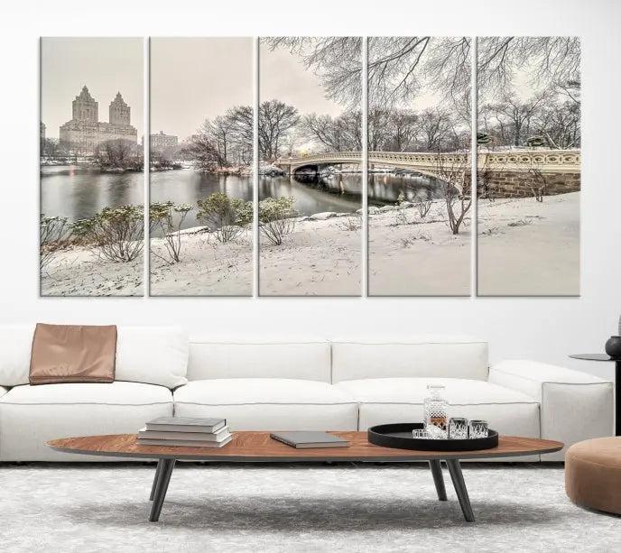 The Bow Bridge in Central Park Canvas Print features a snowy scene with a bridge and city buildings in the background. This museum-quality canvas comes with a UV-protective coating and is ready to hang.