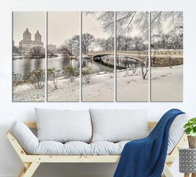 The Bow Bridge in Central Park Canvas Print features a snowy scene with a bridge and city buildings in the background. This museum-quality canvas comes with a UV-protective coating and is ready to hang.