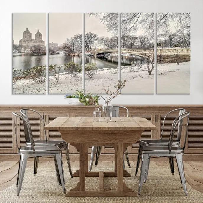 The Bow Bridge in Central Park Canvas Print features a snowy scene with a bridge and city buildings in the background. This museum-quality canvas comes with a UV-protective coating and is ready to hang.