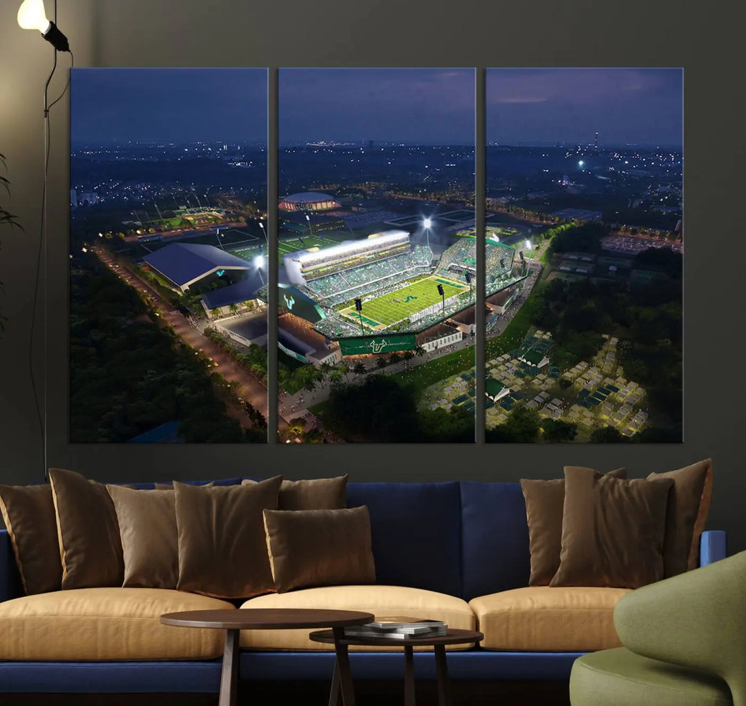 A living room showcasing 'The University of South Florida Bulls Football Team Print' as a triptych wall art highlights the Tampa USF Football Stadium under bright lights at night with a gallery-quality finish.