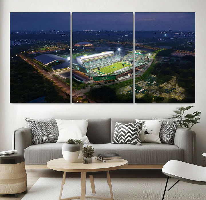 A living room showcasing 'The University of South Florida Bulls Football Team Print' as a triptych wall art highlights the Tampa USF Football Stadium under bright lights at night with a gallery-quality finish.