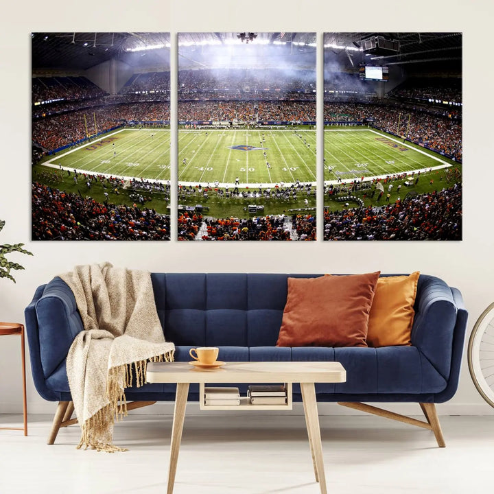 A living room features a striking piece of art on the wall, showcasing high-resolution printing on museum-quality canvas with "The University of Texas at San Antonio Roadrunners Football Team Print - San Antonio Alamodome Wall Art Canvas Print.