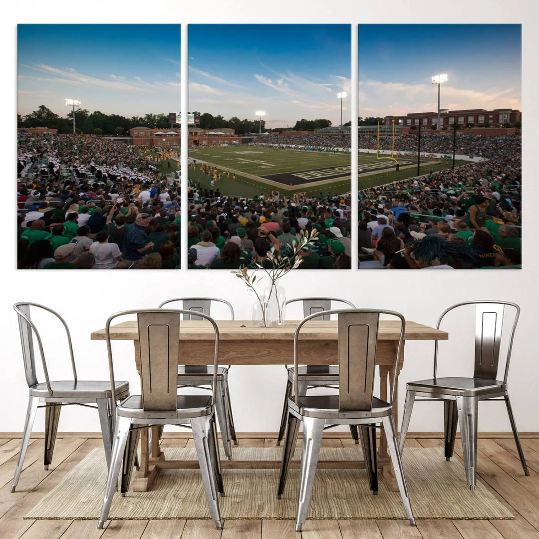 Above the dining table hangs a premium canvas triptych depicting Charlotte Jerry Richardson Stadium, home of the University of Charlotte 49ers Football Team. The scene is alive with a nighttime atmosphere, bustling with a large crowd under bright stadium lights. This stunning art piece is expertly handmade in the USA and adds vibrant energy to your living space.