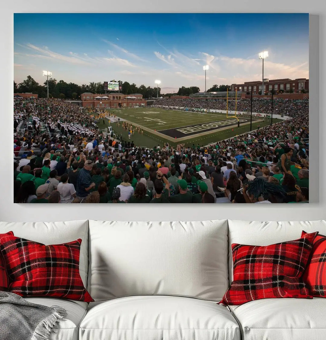 Above the dining table hangs a premium canvas triptych depicting Charlotte Jerry Richardson Stadium, home of the University of Charlotte 49ers Football Team. The scene is alive with a nighttime atmosphere, bustling with a large crowd under bright stadium lights. This stunning art piece is expertly handmade in the USA and adds vibrant energy to your living space.