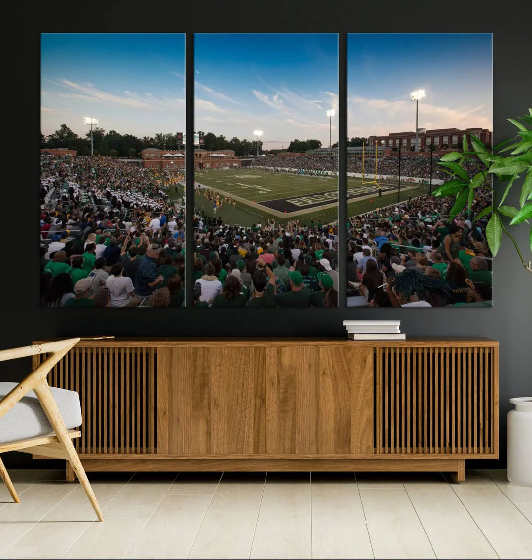 Above the dining table hangs a premium canvas triptych depicting Charlotte Jerry Richardson Stadium, home of the University of Charlotte 49ers Football Team. The scene is alive with a nighttime atmosphere, bustling with a large crowd under bright stadium lights. This stunning art piece is expertly handmade in the USA and adds vibrant energy to your living space.