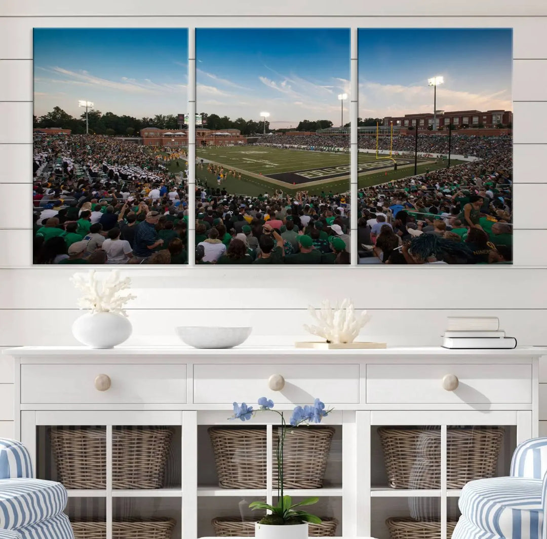 Above the dining table hangs a premium canvas triptych depicting Charlotte Jerry Richardson Stadium, home of the University of Charlotte 49ers Football Team. The scene is alive with a nighttime atmosphere, bustling with a large crowd under bright stadium lights. This stunning art piece is expertly handmade in the USA and adds vibrant energy to your living space.