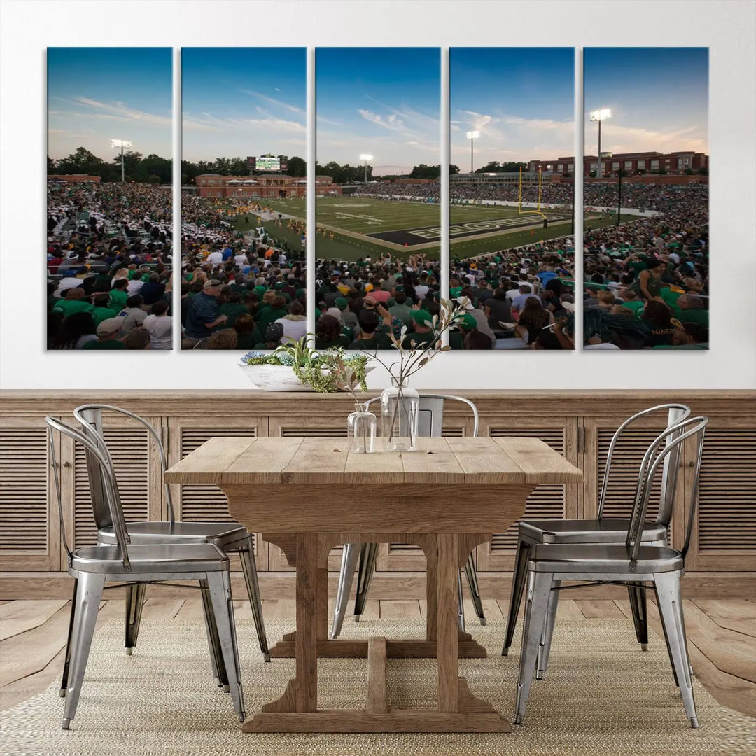 Above the dining table hangs a premium canvas triptych depicting Charlotte Jerry Richardson Stadium, home of the University of Charlotte 49ers Football Team. The scene is alive with a nighttime atmosphere, bustling with a large crowd under bright stadium lights. This stunning art piece is expertly handmade in the USA and adds vibrant energy to your living space.