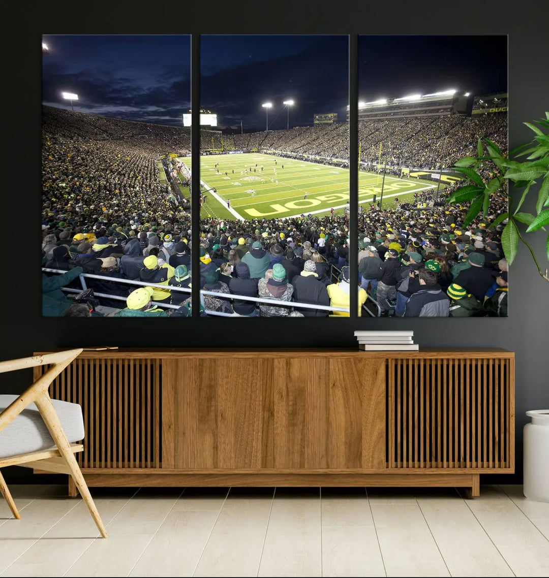 The living room features a triptych of wall art titled "University of Oregon Ducks Football Team Print - Eugene Autzen Stadium Wall Art Canvas Print," which depicts a bustling football stadium at night. Crafted on premium canvas and handmade in the USA, it serves as a striking focal point in the space.