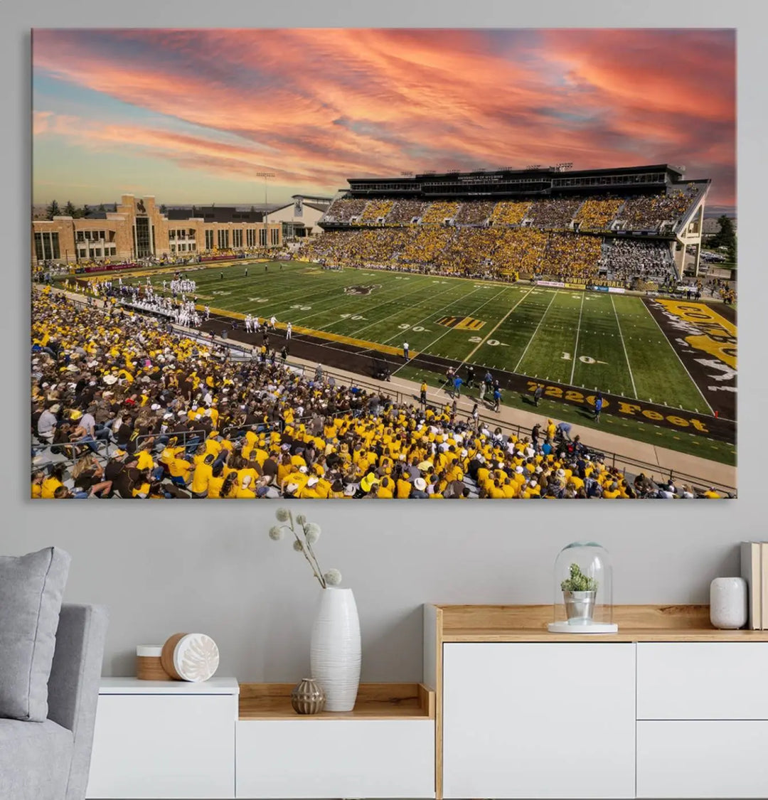 A living room wall showcases a stunning handmade canvas artwork featuring the lively University of Wyoming Cowboys football team at Jonah Field in War Memorial Stadium, beautifully set under a vibrant sunset sky.