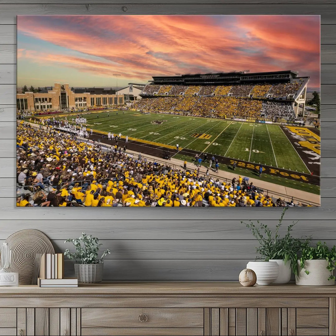 A living room wall showcases a stunning handmade canvas artwork featuring the lively University of Wyoming Cowboys football team at Jonah Field in War Memorial Stadium, beautifully set under a vibrant sunset sky.