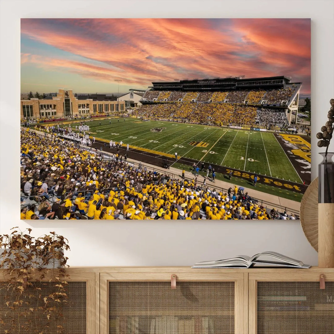 A living room wall showcases a stunning handmade canvas artwork featuring the lively University of Wyoming Cowboys football team at Jonah Field in War Memorial Stadium, beautifully set under a vibrant sunset sky.