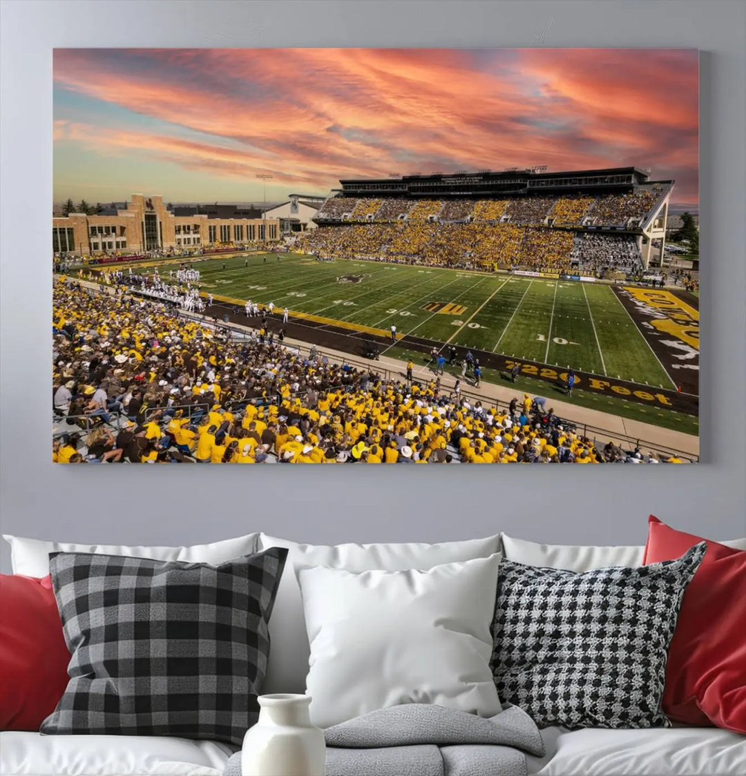 A living room wall showcases a stunning handmade canvas artwork featuring the lively University of Wyoming Cowboys football team at Jonah Field in War Memorial Stadium, beautifully set under a vibrant sunset sky.