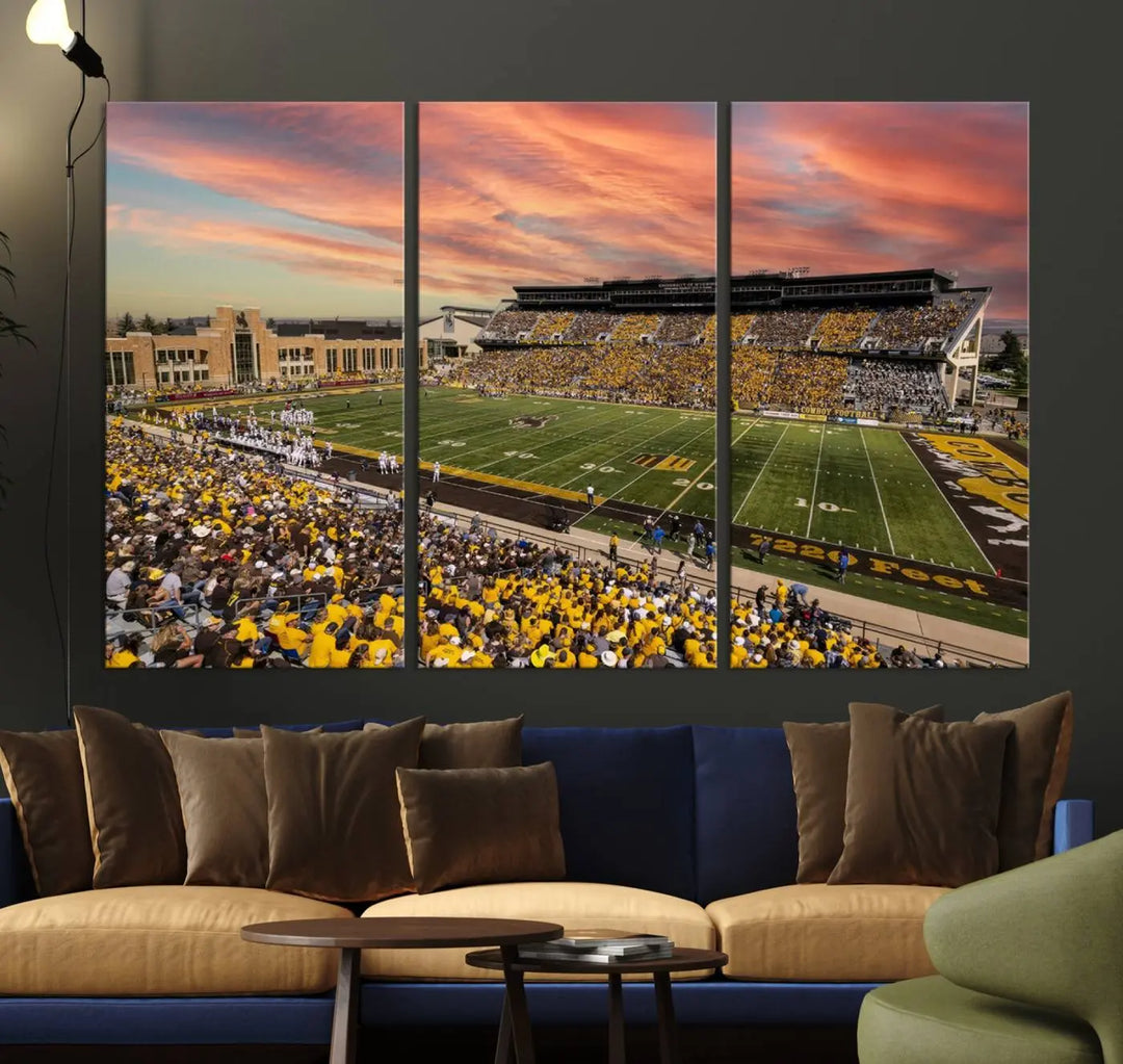 A living room wall showcases a stunning handmade canvas artwork featuring the lively University of Wyoming Cowboys football team at Jonah Field in War Memorial Stadium, beautifully set under a vibrant sunset sky.