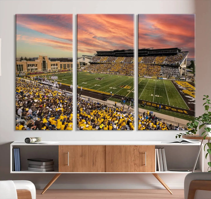 A living room wall showcases a stunning handmade canvas artwork featuring the lively University of Wyoming Cowboys football team at Jonah Field in War Memorial Stadium, beautifully set under a vibrant sunset sky.