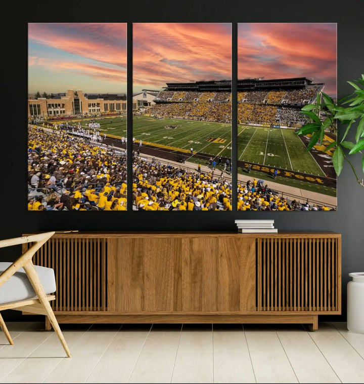 A living room wall showcases a stunning handmade canvas artwork featuring the lively University of Wyoming Cowboys football team at Jonah Field in War Memorial Stadium, beautifully set under a vibrant sunset sky.