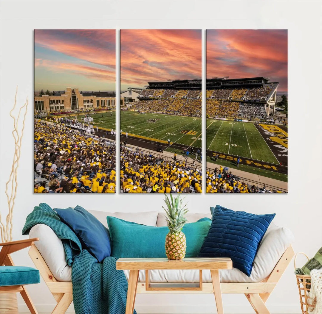 A living room wall showcases a stunning handmade canvas artwork featuring the lively University of Wyoming Cowboys football team at Jonah Field in War Memorial Stadium, beautifully set under a vibrant sunset sky.