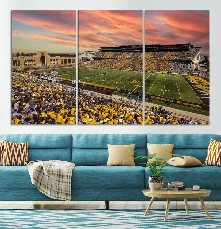 A living room wall showcases a stunning handmade canvas artwork featuring the lively University of Wyoming Cowboys football team at Jonah Field in War Memorial Stadium, beautifully set under a vibrant sunset sky.