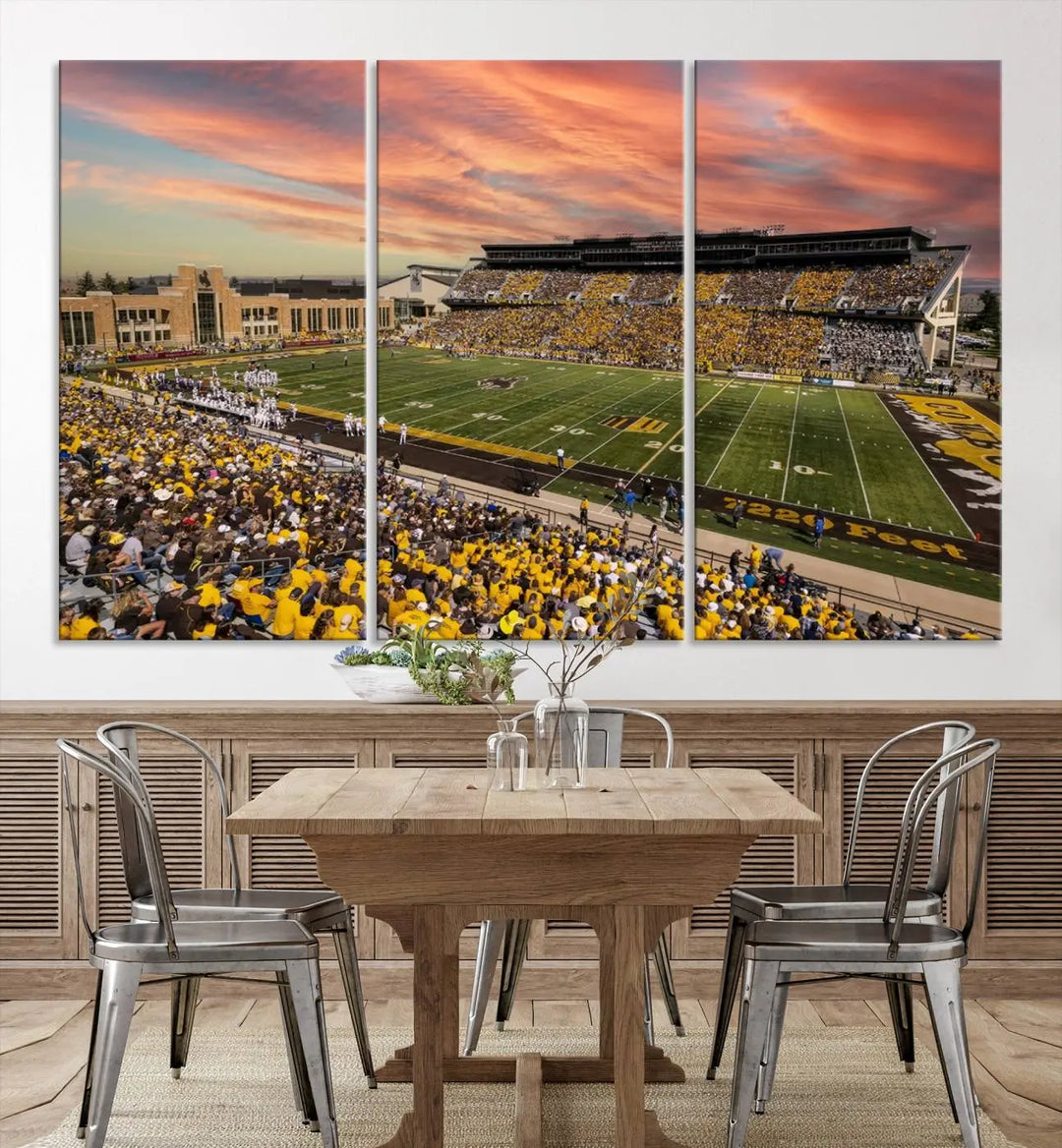 A living room wall showcases a stunning handmade canvas artwork featuring the lively University of Wyoming Cowboys football team at Jonah Field in War Memorial Stadium, beautifully set under a vibrant sunset sky.