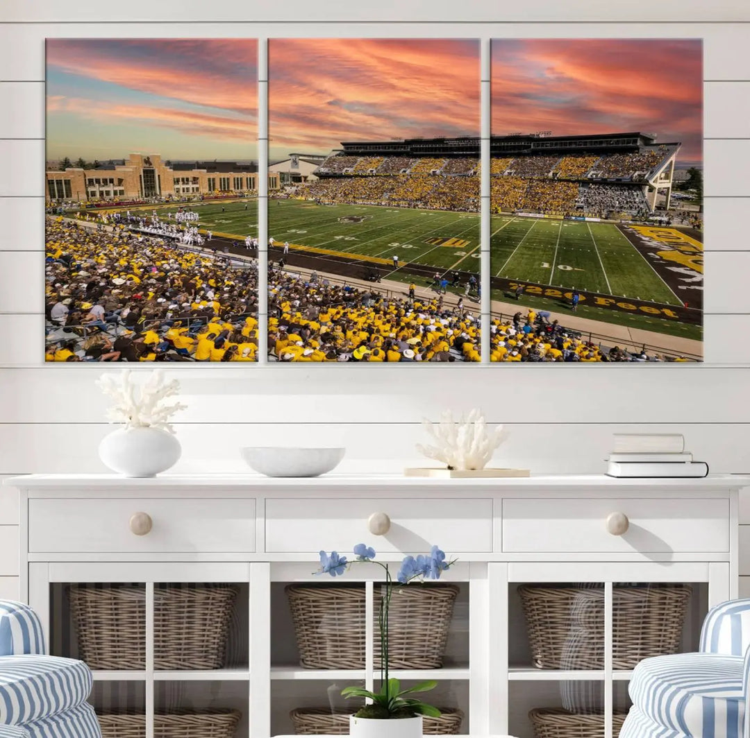 A living room wall showcases a stunning handmade canvas artwork featuring the lively University of Wyoming Cowboys football team at Jonah Field in War Memorial Stadium, beautifully set under a vibrant sunset sky.