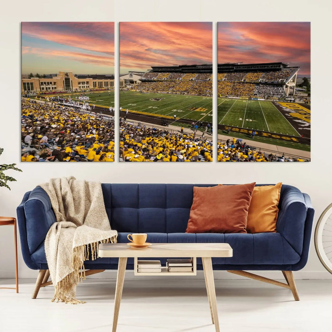 A living room wall showcases a stunning handmade canvas artwork featuring the lively University of Wyoming Cowboys football team at Jonah Field in War Memorial Stadium, beautifully set under a vibrant sunset sky.