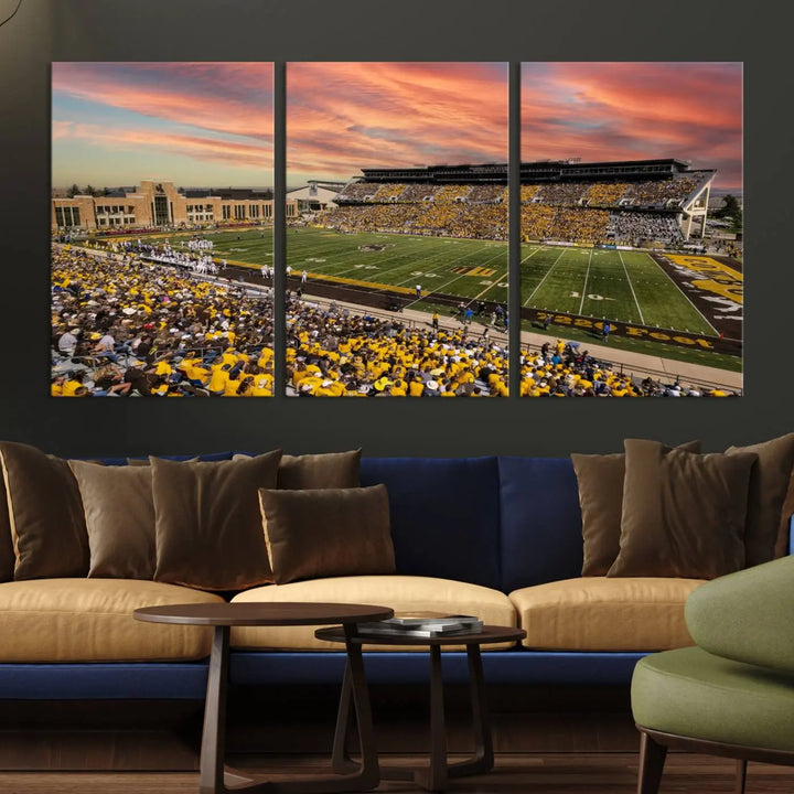 A living room wall showcases a stunning handmade canvas artwork featuring the lively University of Wyoming Cowboys football team at Jonah Field in War Memorial Stadium, beautifully set under a vibrant sunset sky.