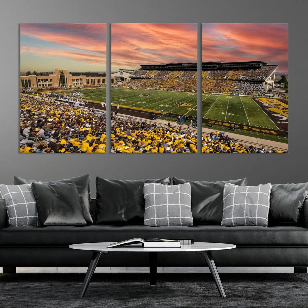 A living room wall showcases a stunning handmade canvas artwork featuring the lively University of Wyoming Cowboys football team at Jonah Field in War Memorial Stadium, beautifully set under a vibrant sunset sky.