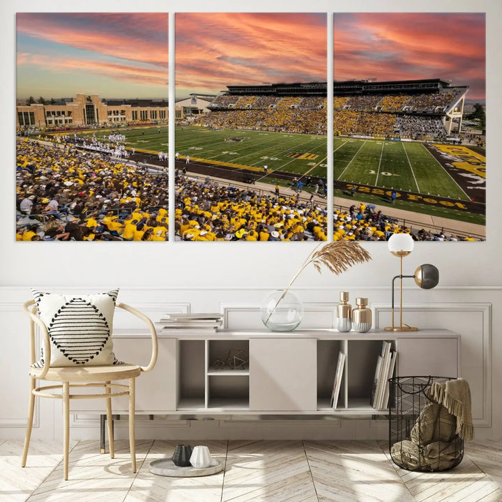 A living room wall showcases a stunning handmade canvas artwork featuring the lively University of Wyoming Cowboys football team at Jonah Field in War Memorial Stadium, beautifully set under a vibrant sunset sky.