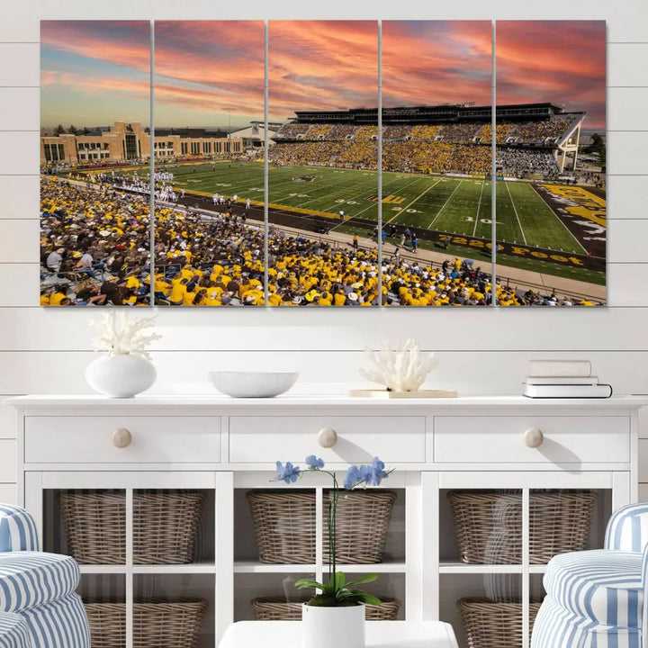 A living room wall showcases a stunning handmade canvas artwork featuring the lively University of Wyoming Cowboys football team at Jonah Field in War Memorial Stadium, beautifully set under a vibrant sunset sky.