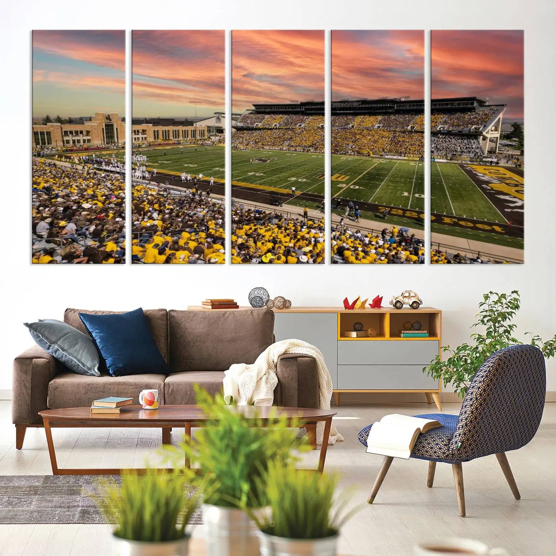 A living room wall showcases a stunning handmade canvas artwork featuring the lively University of Wyoming Cowboys football team at Jonah Field in War Memorial Stadium, beautifully set under a vibrant sunset sky.