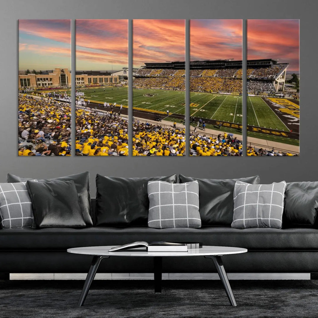 A living room wall showcases a stunning handmade canvas artwork featuring the lively University of Wyoming Cowboys football team at Jonah Field in War Memorial Stadium, beautifully set under a vibrant sunset sky.