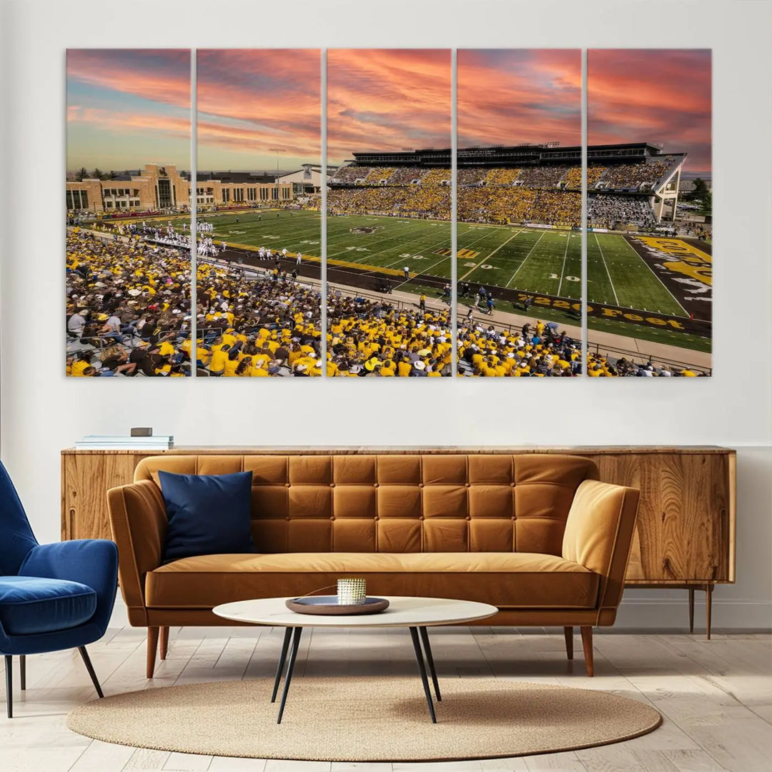 A living room wall showcases a stunning handmade canvas artwork featuring the lively University of Wyoming Cowboys football team at Jonah Field in War Memorial Stadium, beautifully set under a vibrant sunset sky.