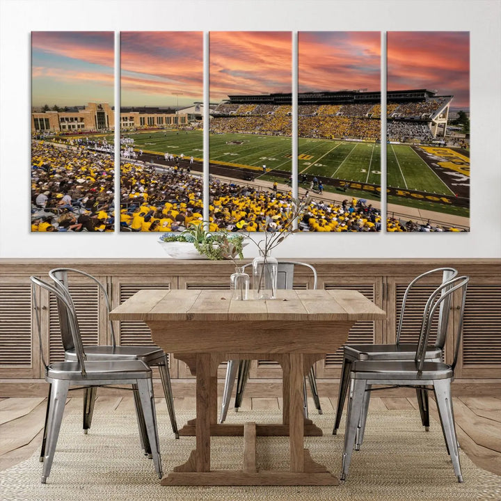 A living room wall showcases a stunning handmade canvas artwork featuring the lively University of Wyoming Cowboys football team at Jonah Field in War Memorial Stadium, beautifully set under a vibrant sunset sky.