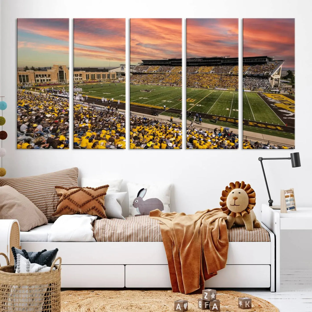 A living room wall showcases a stunning handmade canvas artwork featuring the lively University of Wyoming Cowboys football team at Jonah Field in War Memorial Stadium, beautifully set under a vibrant sunset sky.