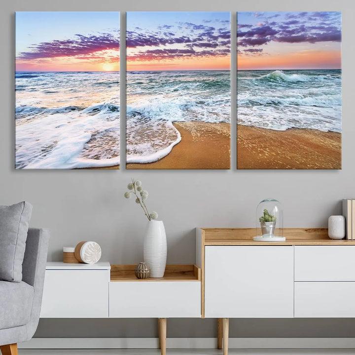 The "Vivid Sunset Ocean Waves Wall Art" hangs on the wall, capturing the serene beauty of the sea. This coastal beach canvas print triptych perfectly enhances living rooms and relaxation spaces.