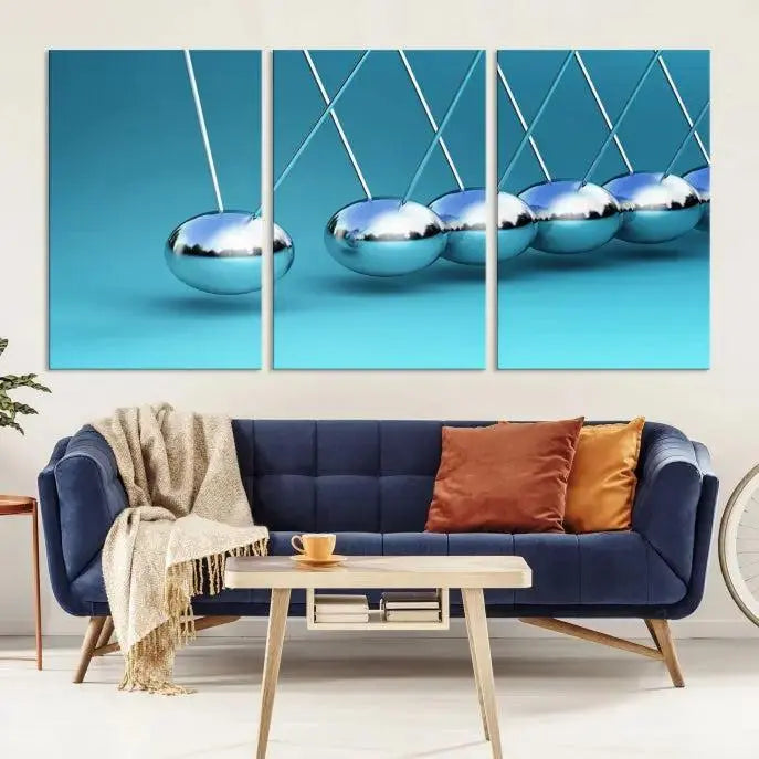 The Wall Art Newton's Cradle Canvas Print is displayed as a triptych on a teal background. Each piece is gallery-wrapped and crafted on museum-quality canvases with a UV-protective coating, ensuring lasting vibrancy and protection.