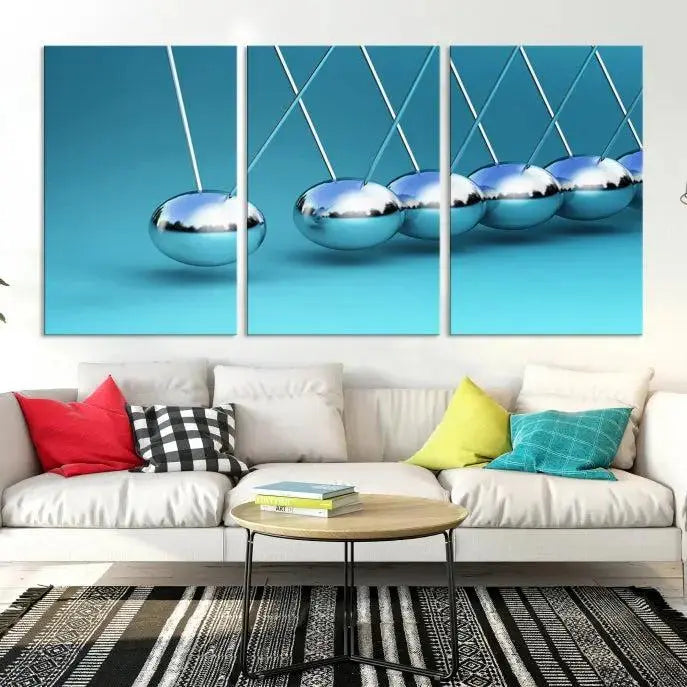 The Wall Art Newton's Cradle Canvas Print is displayed as a triptych on a teal background. Each piece is gallery-wrapped and crafted on museum-quality canvases with a UV-protective coating, ensuring lasting vibrancy and protection.