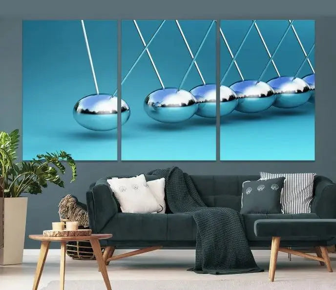 The Wall Art Newton's Cradle Canvas Print is displayed as a triptych on a teal background. Each piece is gallery-wrapped and crafted on museum-quality canvases with a UV-protective coating, ensuring lasting vibrancy and protection.